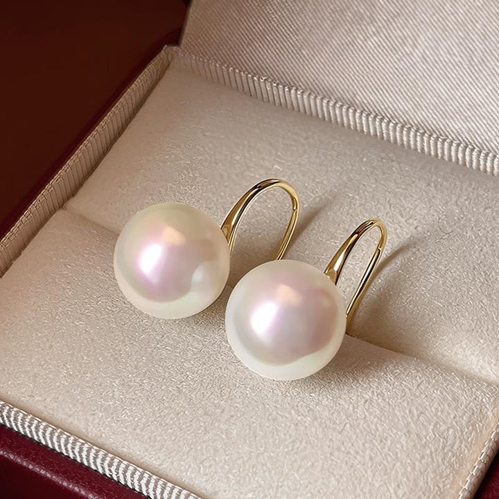 Close-up image of 8mm round white freshwater pearl earrings with a gold-tone stiletto heel-inspired hook design and pavé-set crystals.