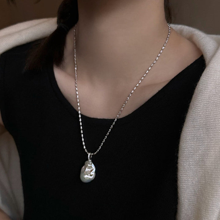 Close-up image of a silver-tone chunky chain necklace with a toggle clasp and a unique baroque freshwater pearl pendant.