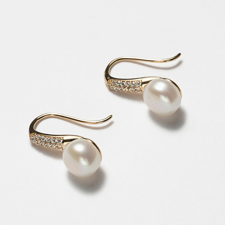 Close-up image of 8mm round white freshwater pearl earrings with a gold-tone stiletto heel-inspired hook design and pavé-set crystals.